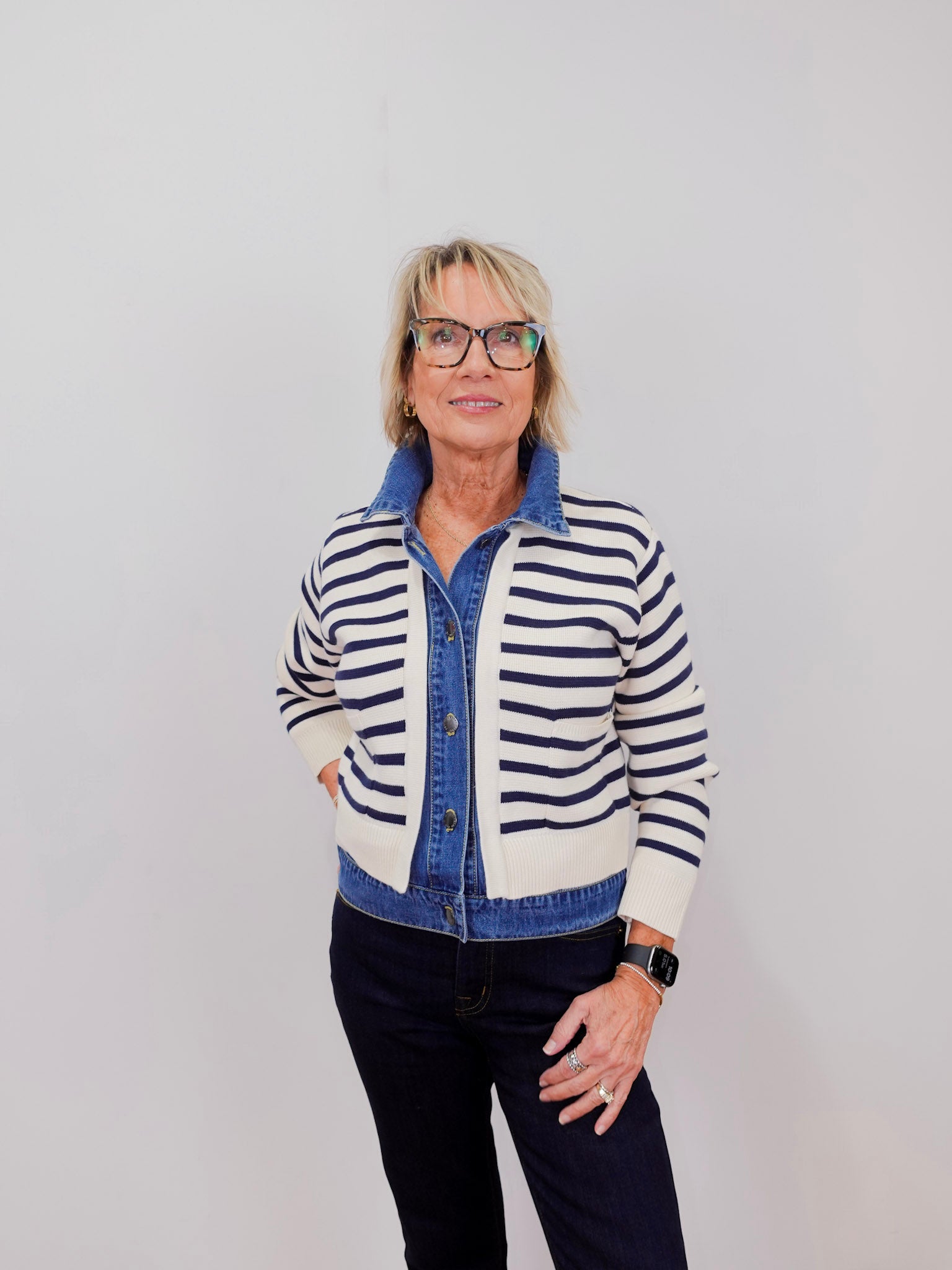 Woman wearing a striped cardigan over a denim shirt with a plain background