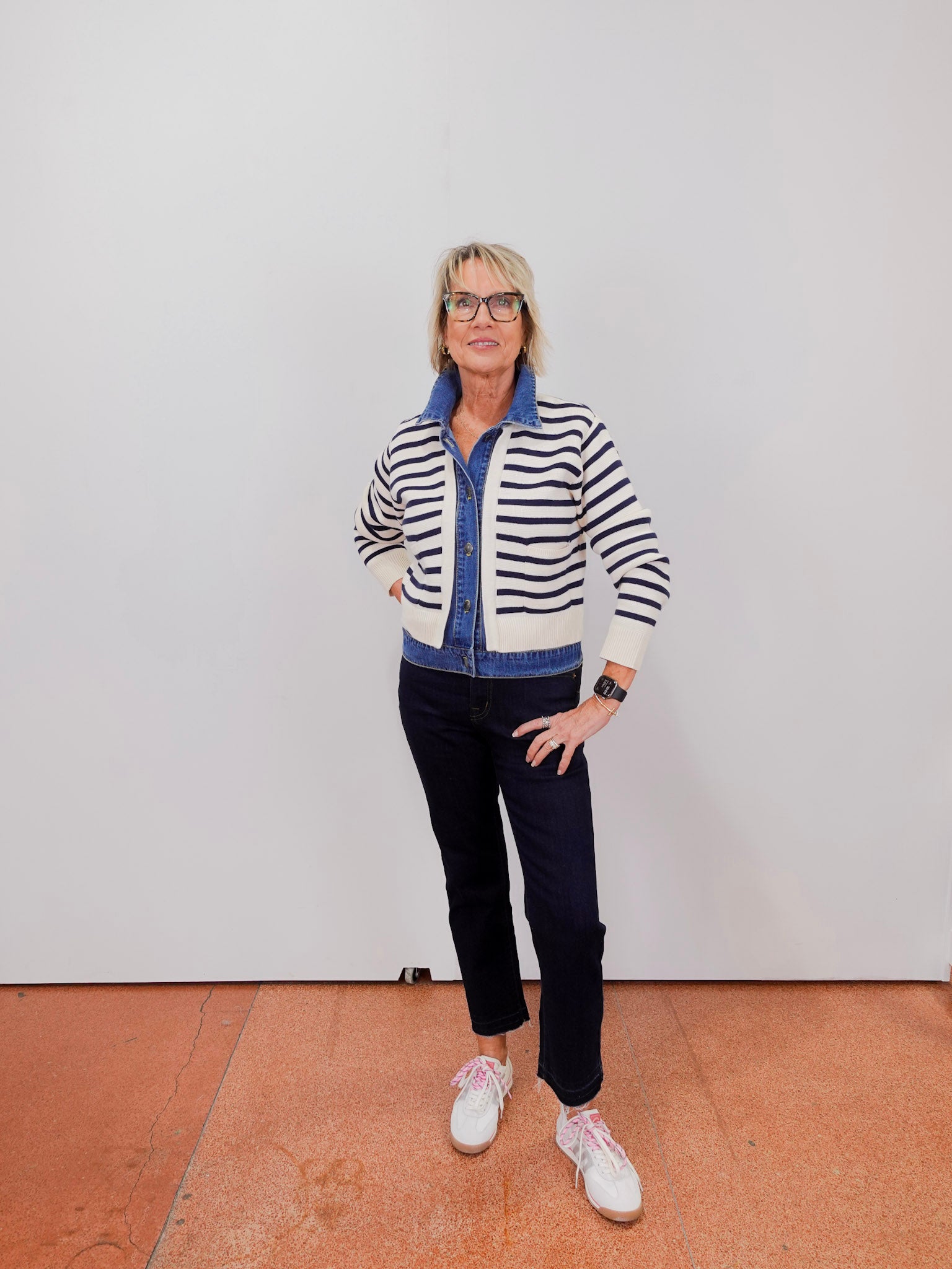 Person wearing a striped sweater and dark pants standing against a white wall.