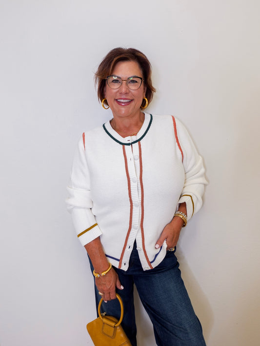 Woman wearing a white cardigan with colorful accents against a plain background