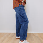 Person wearing blue jeans and a patterned shirt on a plain background