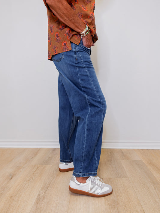 Person wearing blue jeans and a patterned shirt on a plain background