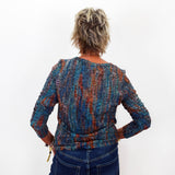 A woman viewed from behind wearing a long-sleeve textured knit top with a multicolor abstract pattern in blue, orange, and purple, paired with dark blue jeans against a plain white background.