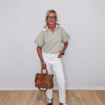 Person wearing a striped shirt, white pants, and holding a brown bag against a plain background