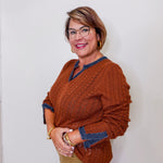 Woman wearing a brown sweater with blue trim against a white wall