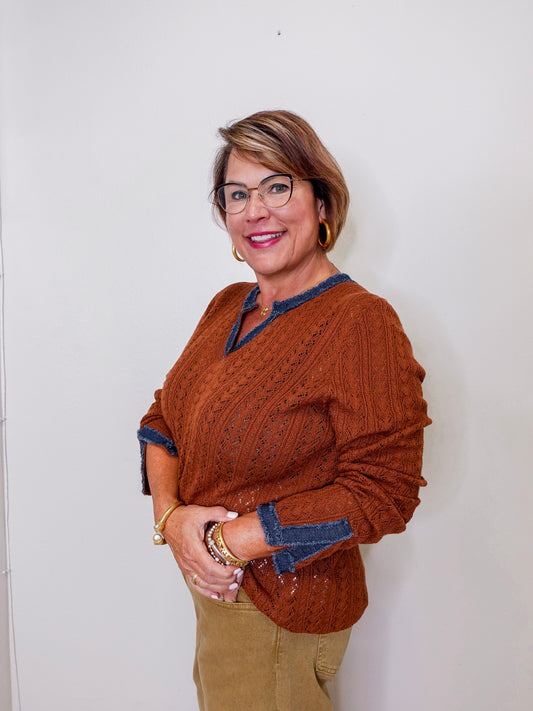 Woman wearing a brown sweater with blue trim against a white wall