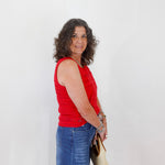 Woman wearing a red sleeveless top and blue jeans, holding a beige handbag against a white background