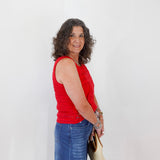Woman wearing a red sleeveless top and blue jeans, holding a beige handbag against a white background
