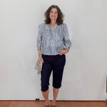 Woman wearing a striped shirt and dark pants against a white wall.