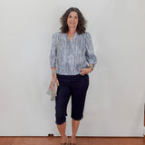 Woman wearing a striped shirt and dark pants against a white wall.
