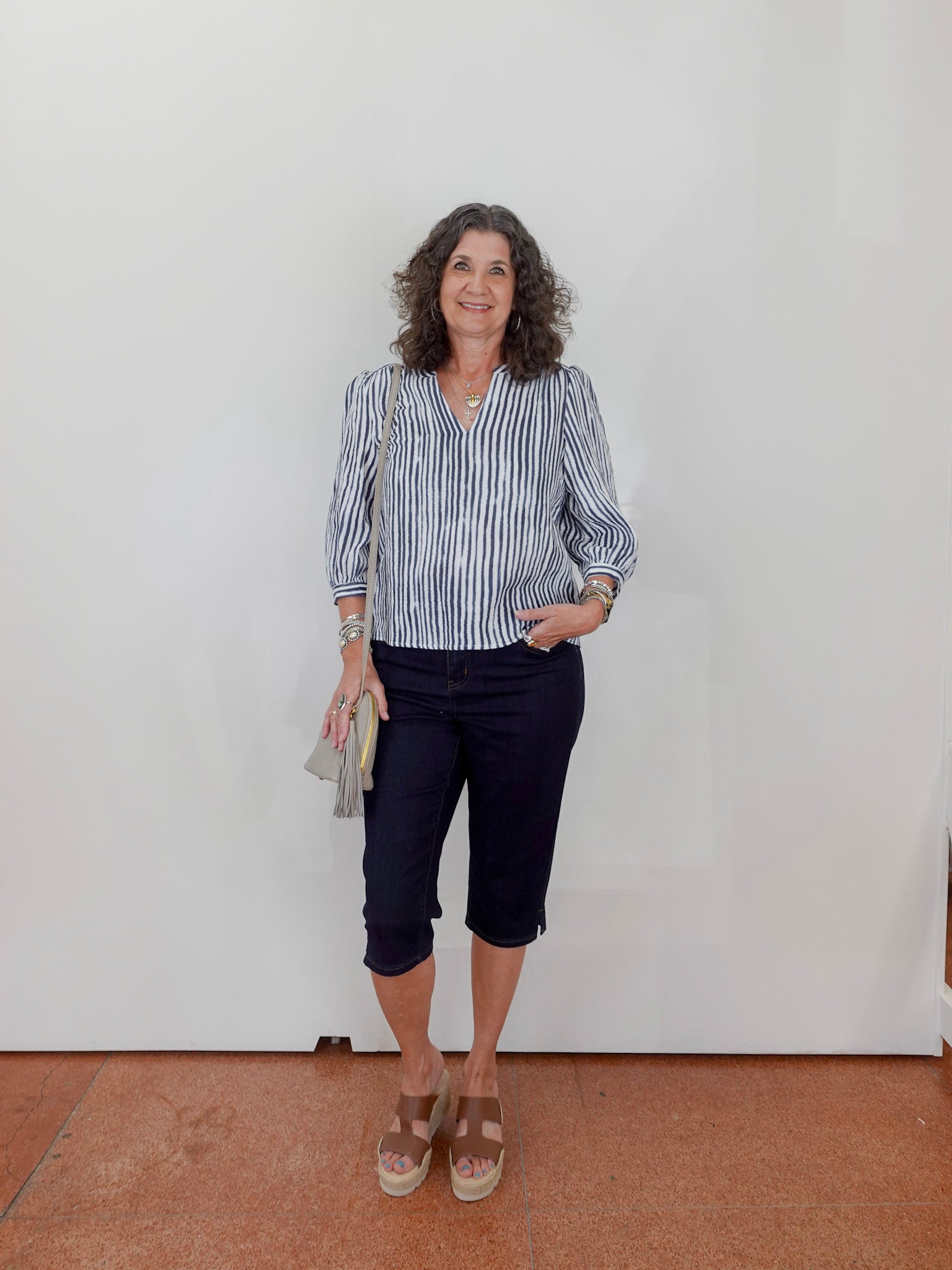 Woman wearing a striped shirt and dark pants against a white wall.