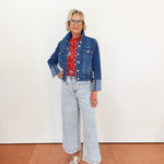 Person wearing a blue denim jacket, red patterned shirt, and light blue jeans on a white background