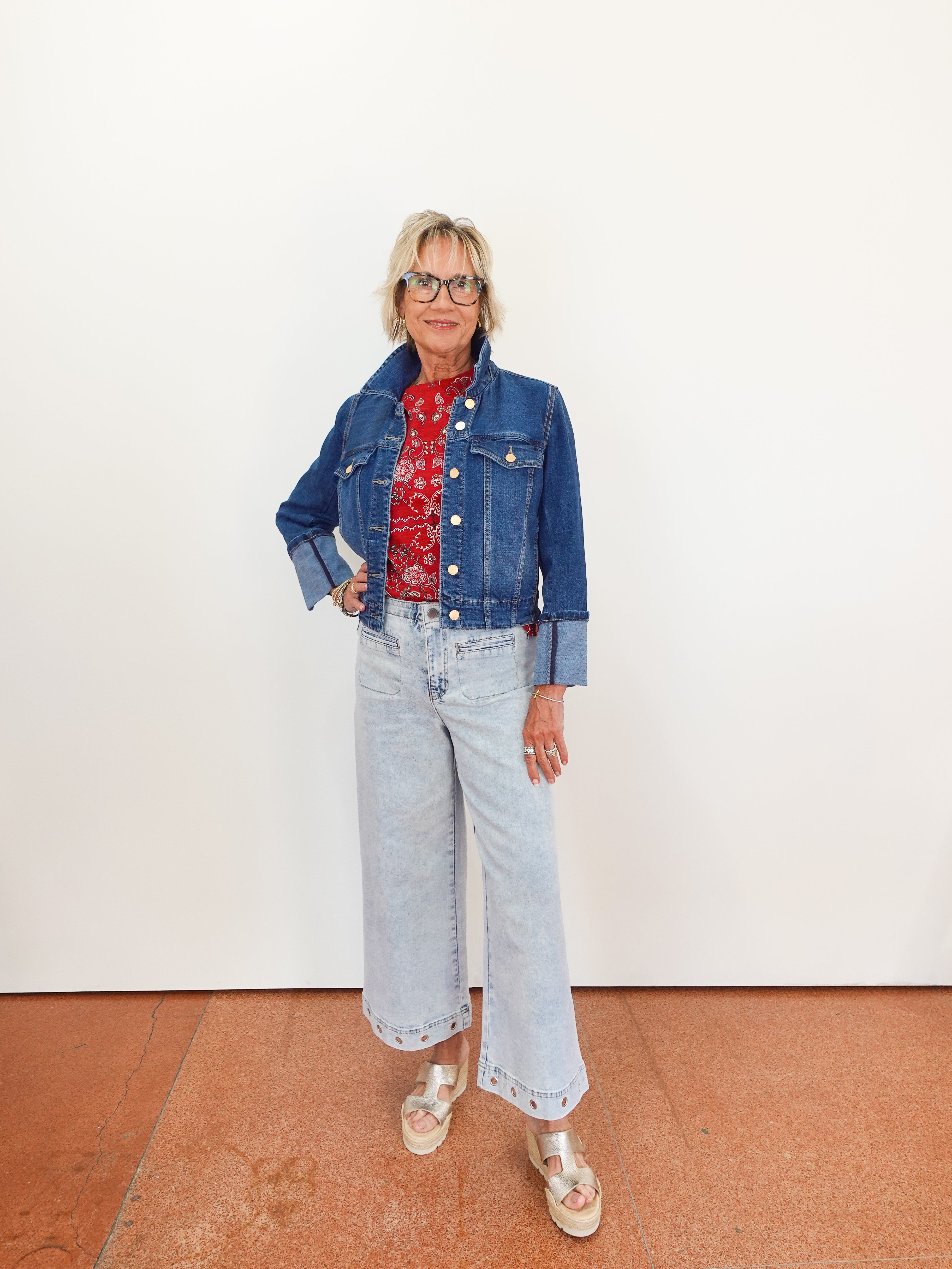 Person wearing a blue denim jacket, red patterned shirt, and light blue jeans on a white background