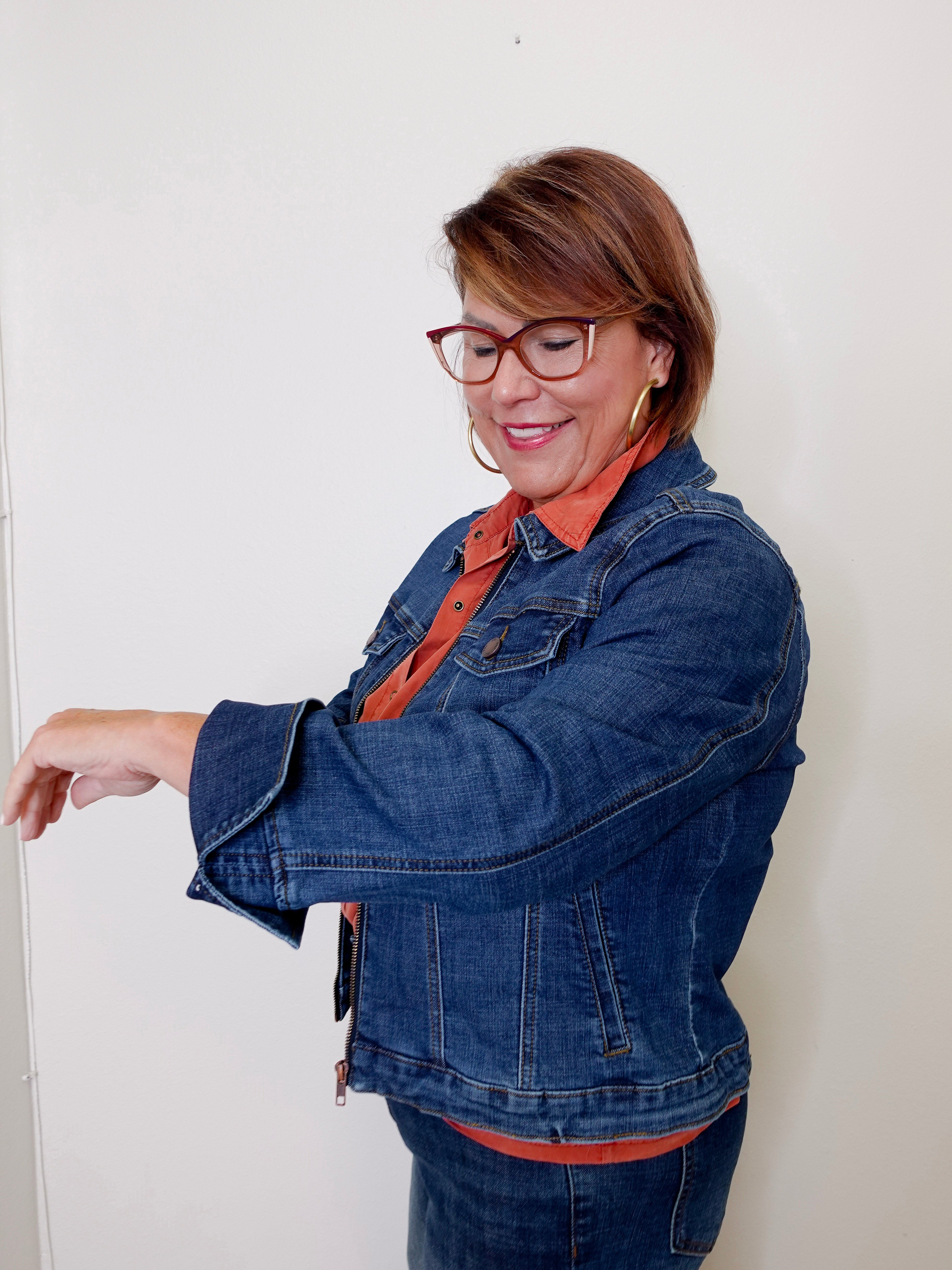 Woman wearing a blue denim jacket and orange shirt against a white background