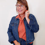 Woman wearing a blue denim jacket over a rust-colored shirt against a white background