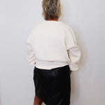 Person wearing a white sweater and black skirt against a plain white wall.