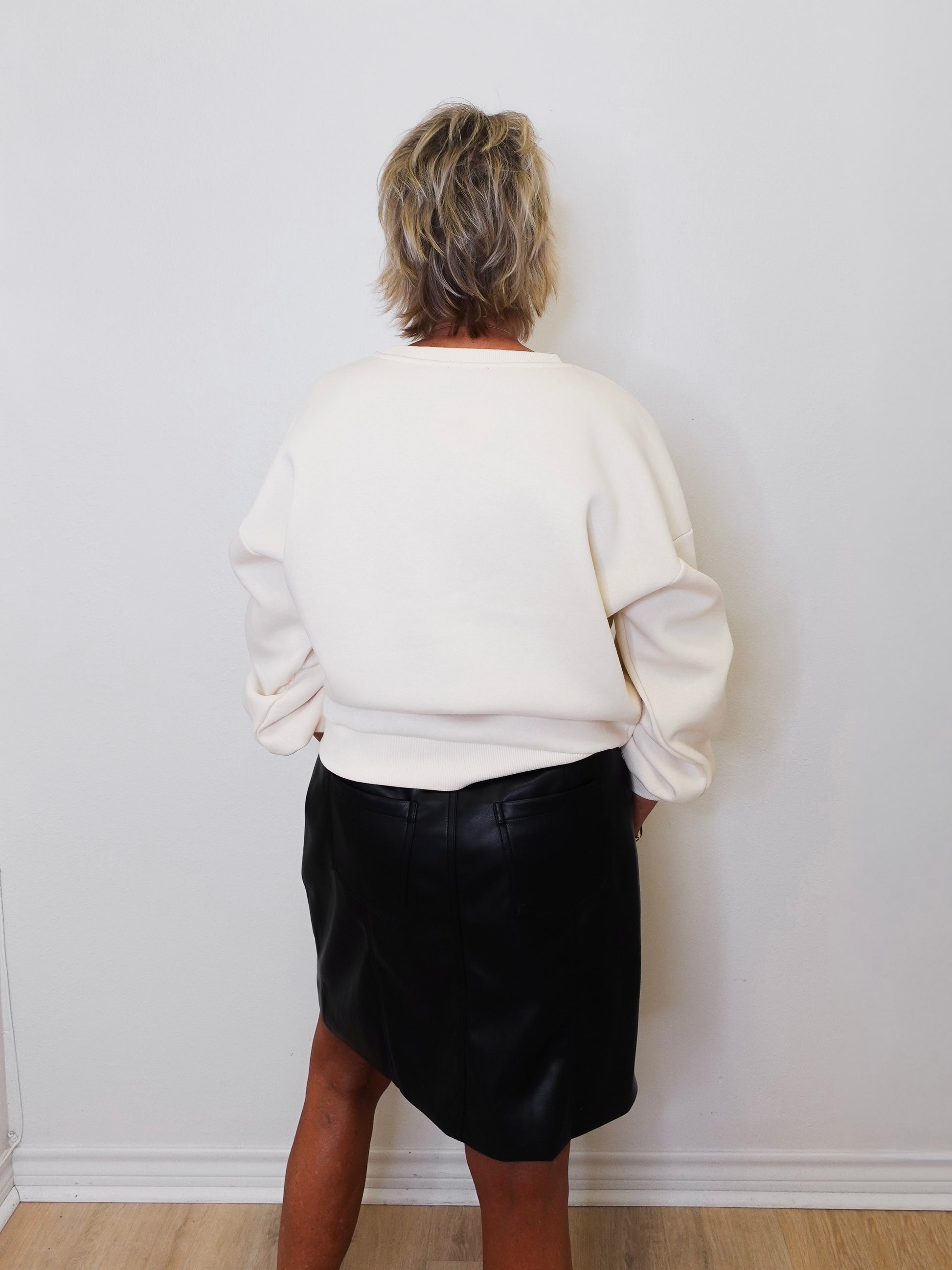 Person wearing a white sweater and black skirt against a plain white wall.