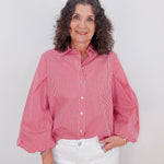 Woman wearing a red checkered shirt and white pants against a plain background