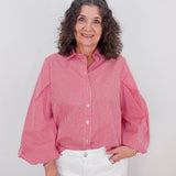 Woman wearing a red checkered shirt and white pants against a plain background
