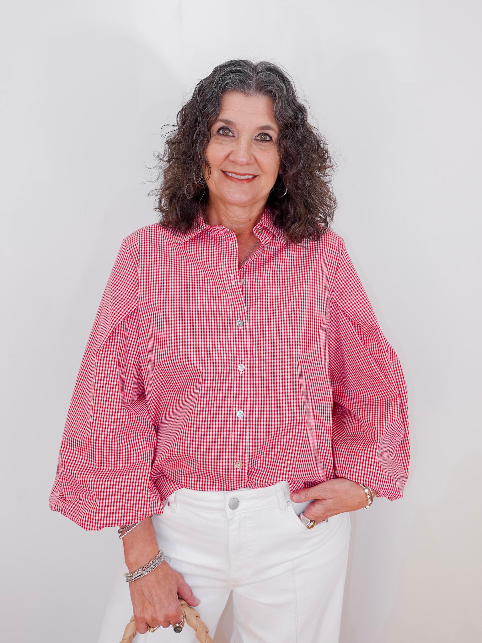Woman wearing a red checkered shirt and white pants against a plain background