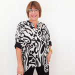 Woman wearing a black and white patterned shirt with a red handbag against a white background