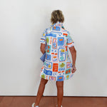 Person wearing a colorful patterned dress standing against a white wall.