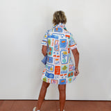Person wearing a colorful patterned dress standing against a white wall.