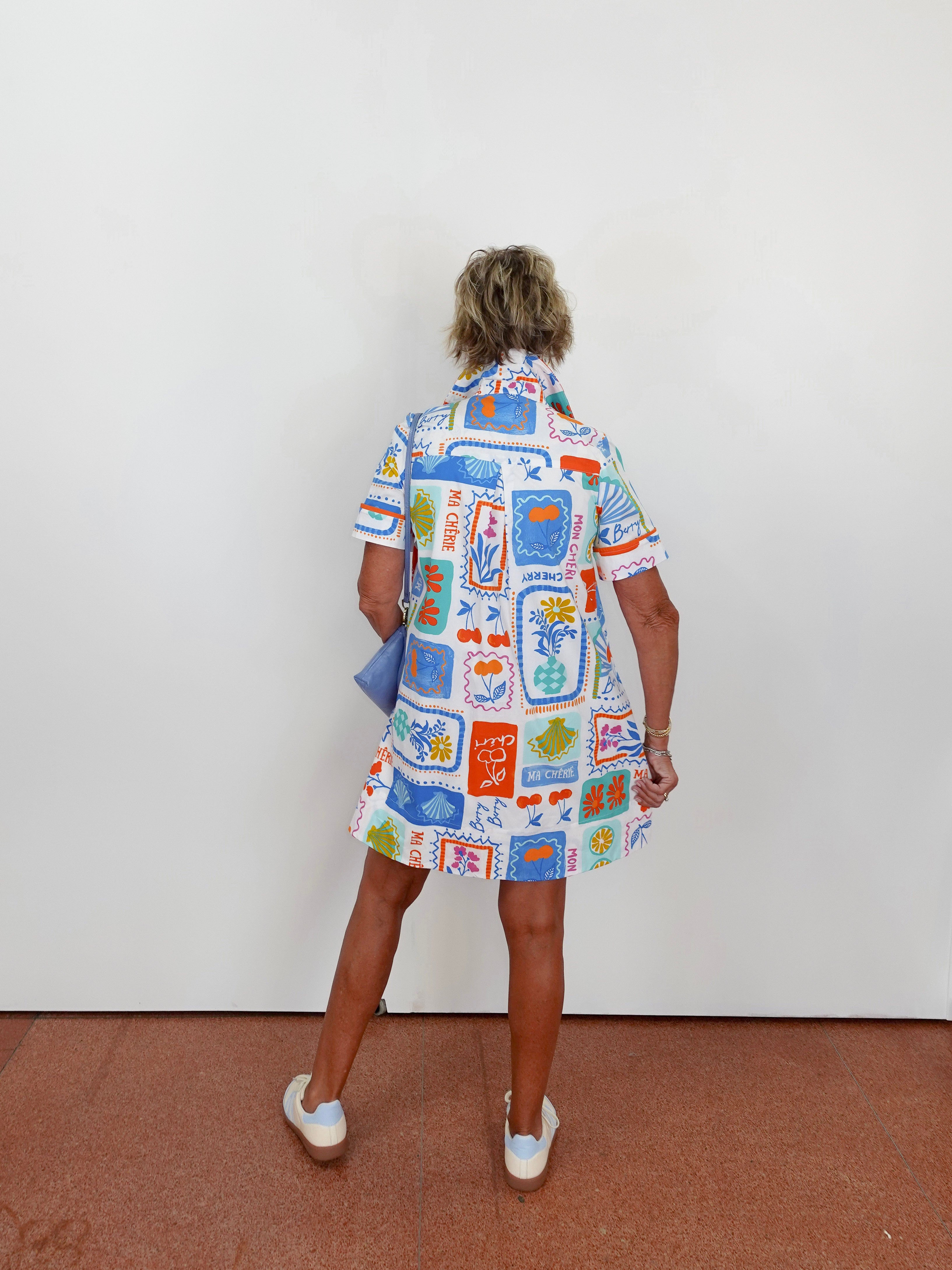 Person wearing a colorful patterned dress standing against a white wall.