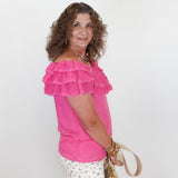 Woman wearing a pink ruffled top and floral pants, holding a beige handbag on a white background