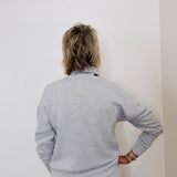 Person wearing a gray outfit against a white wall
