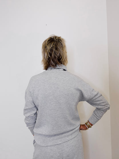 Person wearing a gray outfit against a white wall