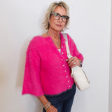Woman wearing a bright pink cardigan holding a white handbag against a plain background