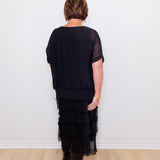 Person wearing a black outfit with a layered skirt against a white wall.