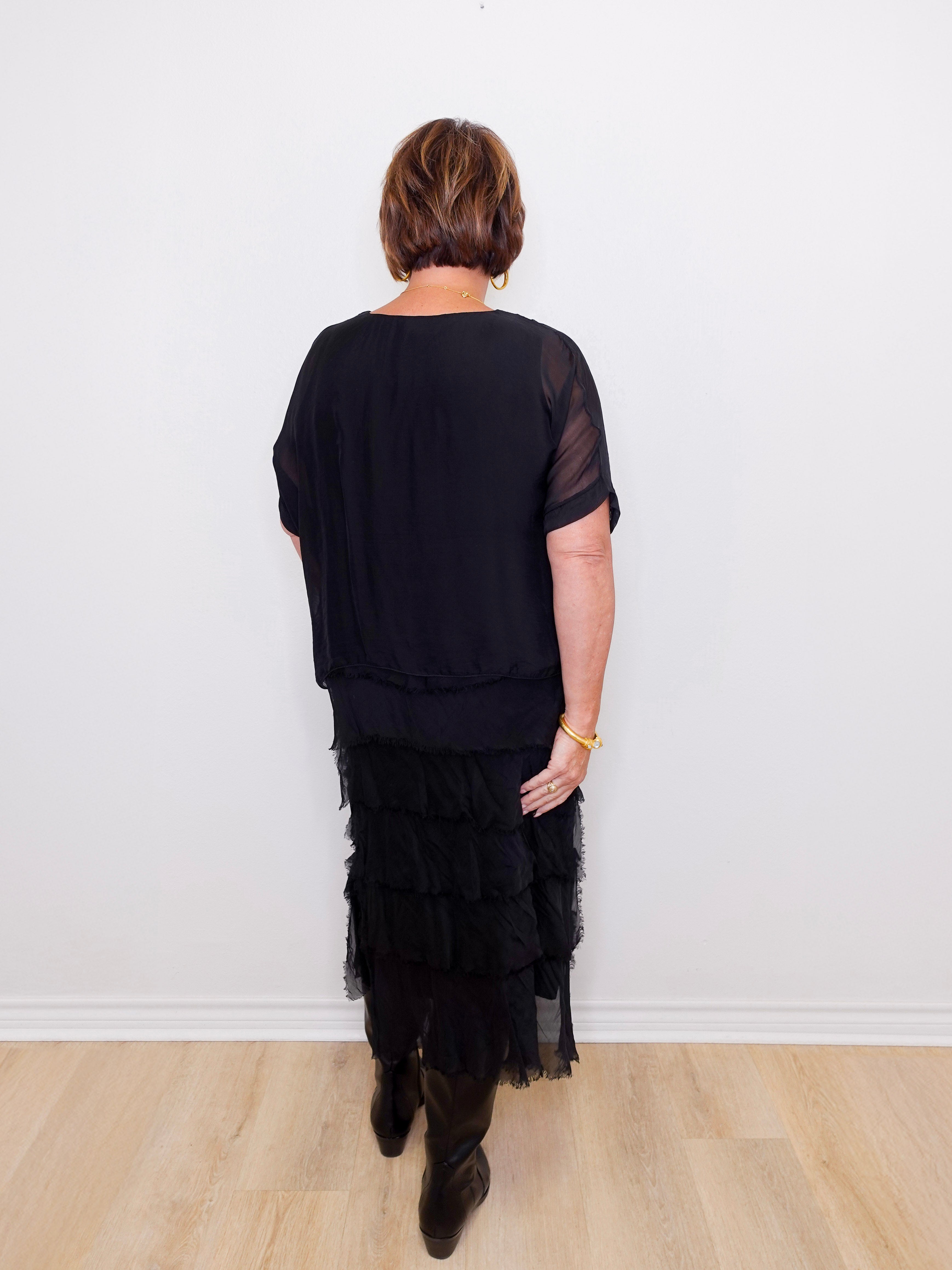 Person wearing a black outfit with a layered skirt against a white wall.