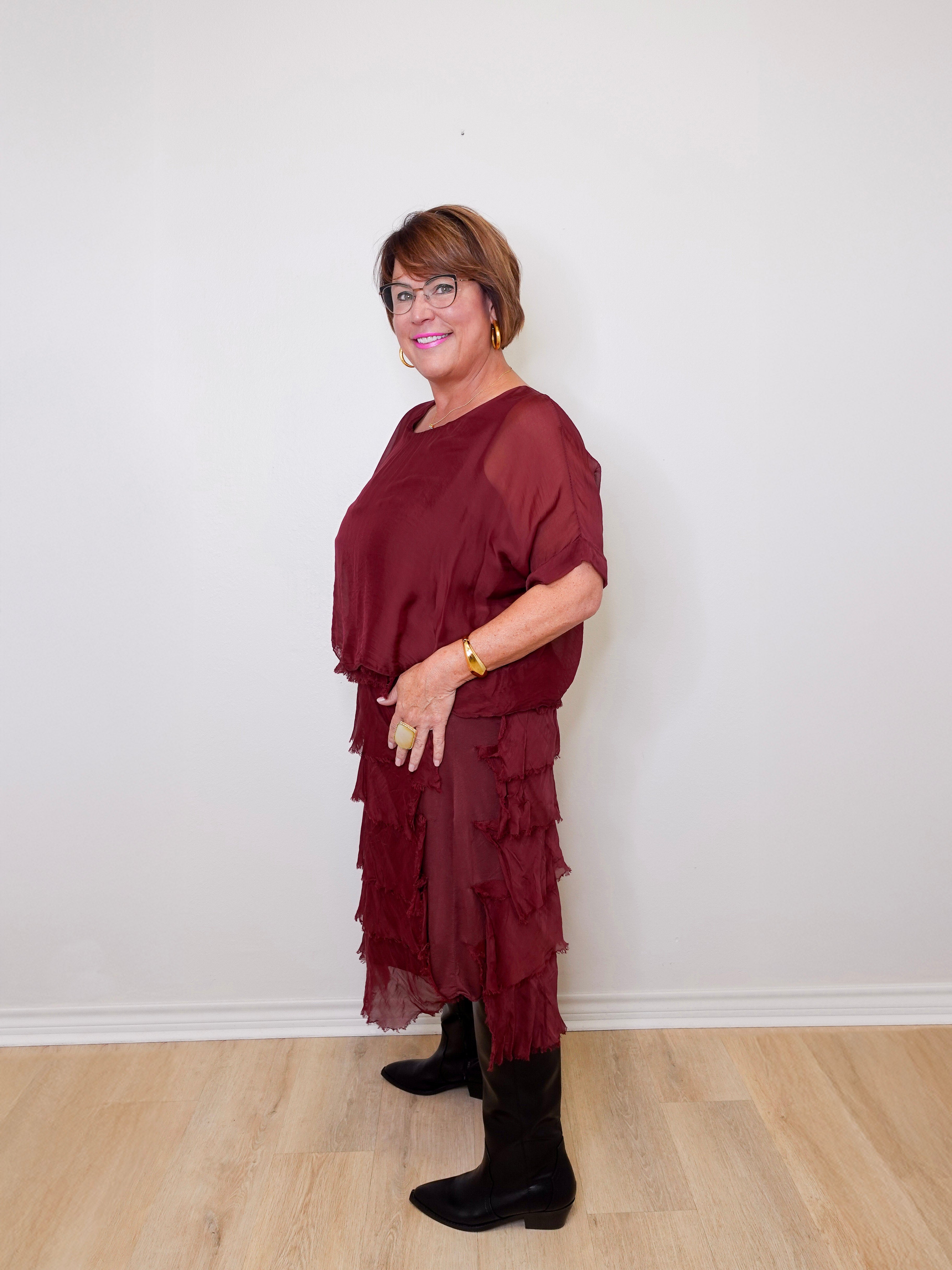 Woman wearing a burgundy dress with ruffled layers against a white wall.