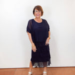 Woman wearing the Gail tiered ruffle dress in navy with a flowy silhouette and layered ruffle details.