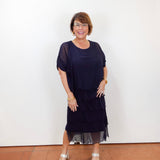 Woman wearing the Gail tiered ruffle dress in navy with a flowy silhouette and layered ruffle details.