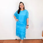 Woman wearing the Gail tiered ruffle dress in turquoise with a flowy silhouette and layered ruffle details.