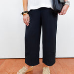 Person wearing black pants and white top, holding a black handbag on a white background