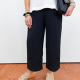 Person wearing black pants and white top, holding a black handbag on a white background