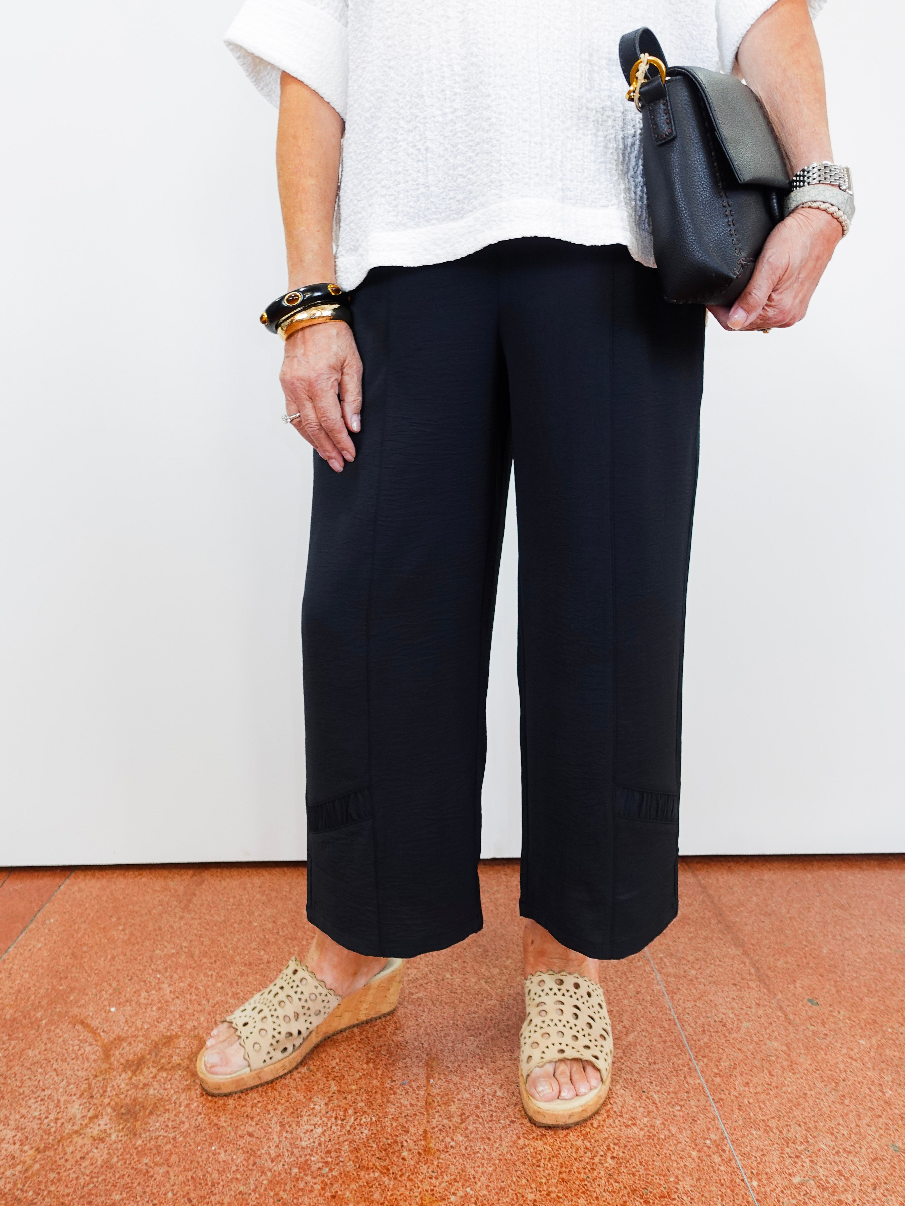Person wearing black pants and white top, holding a black handbag on a white background