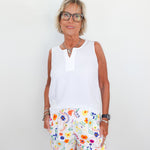 Woman wearing a white sleeveless top and colorful floral shorts against a plain background