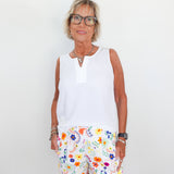 Woman wearing a white sleeveless top and colorful floral shorts against a plain background