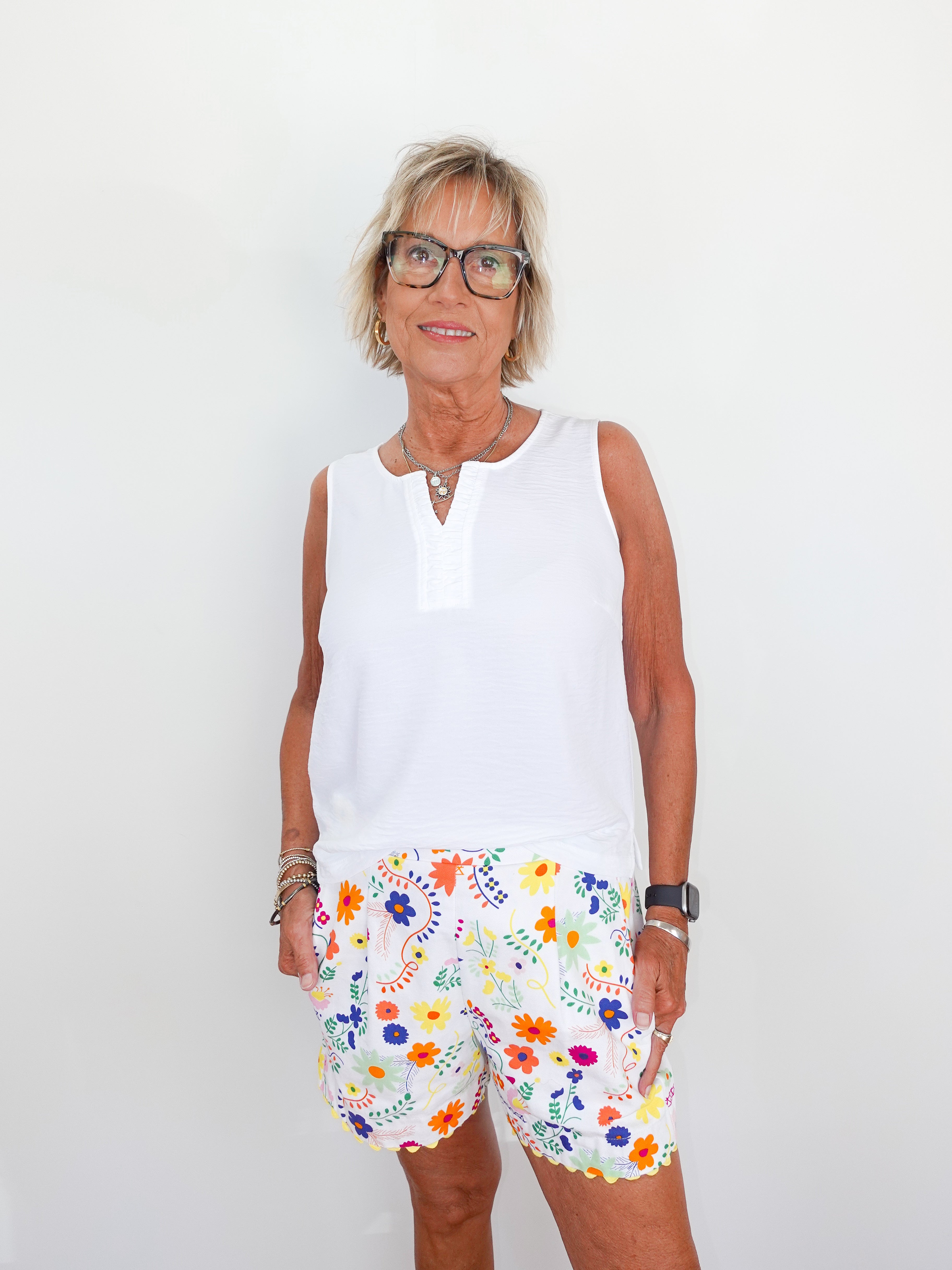 Woman wearing a white sleeveless top and colorful floral shorts against a plain background