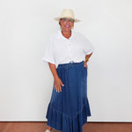 Woman wearing a white shirt, blue denim skirt, and beige hat against a white background