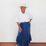 Woman wearing a white shirt, blue denim skirt, and beige hat against a white background