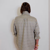 Person wearing a patterned shirt and white pants against a plain wall.