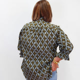 A woman viewed from behind wearing a long-sleeve button-up blouse with a green and gray geometric pattern, paired with light blue jeans, against a plain white background.