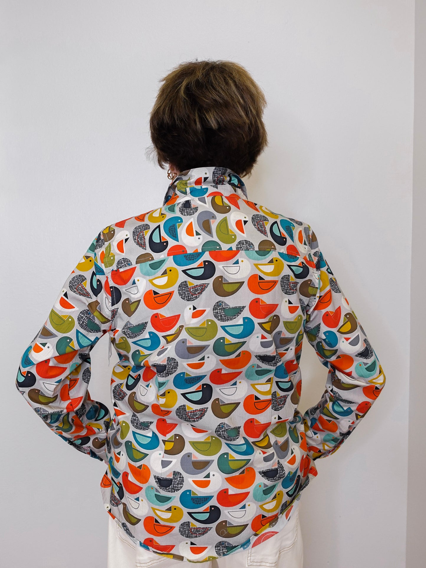 Person wearing a colorful bird-patterned shirt against a white background