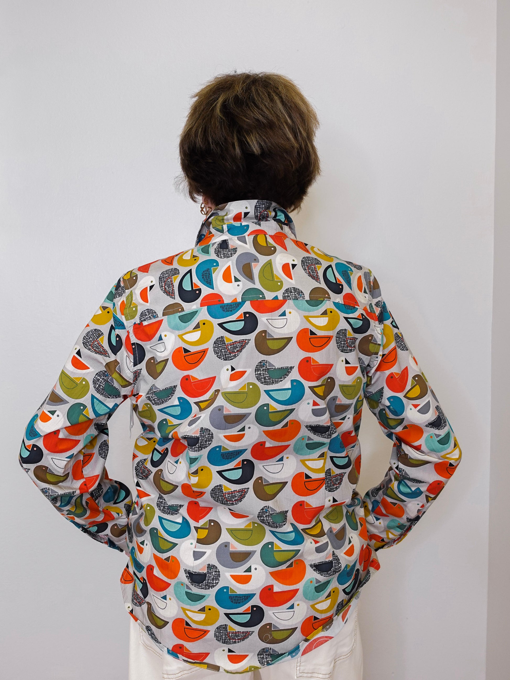 Person wearing a colorful bird-patterned shirt against a white background
