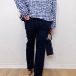 Person wearing a blue plaid shirt and dark jeans against a white wall.